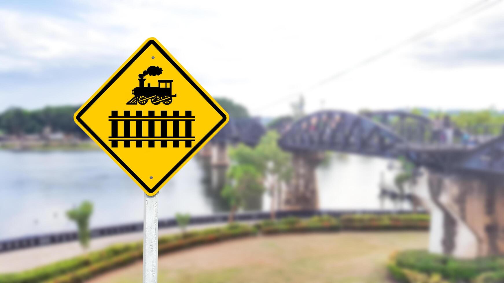 A black train and railway crossing symbol is prominently displayed on a bright yellow sign. photo