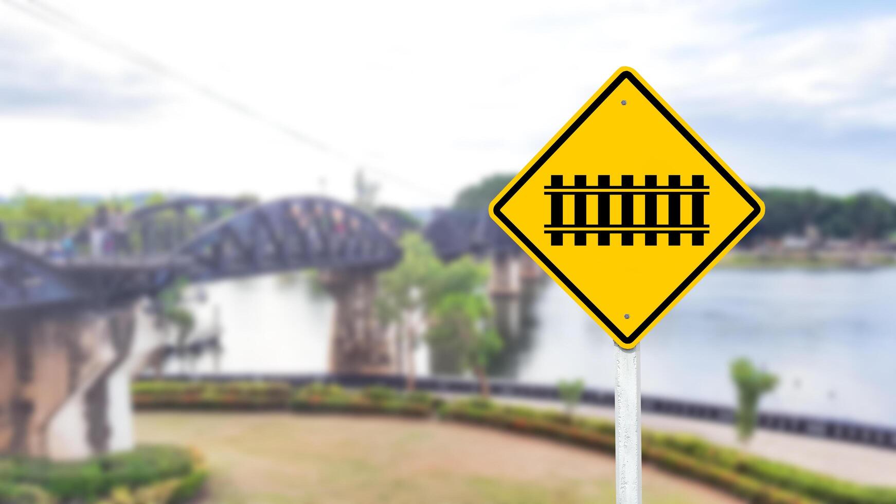 A black train and railway crossing symbol is prominently displayed on a bright yellow sign. photo