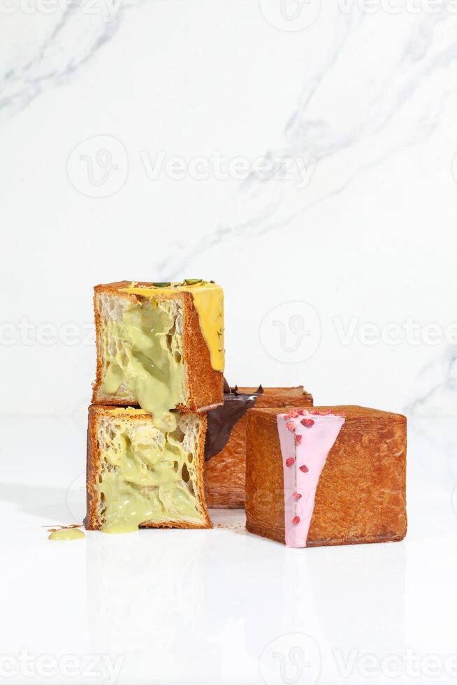Sliced cube shaped croissant with pistachio cream and two whole with berry glaze and chocolate ganache photo