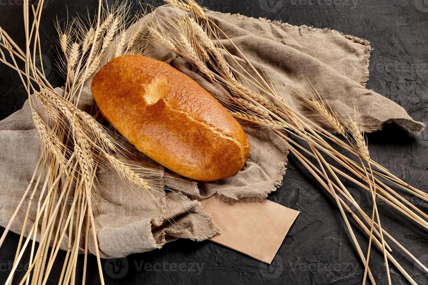 Wheat bread loaf on coarse burlap with ears of wheat on black background photo