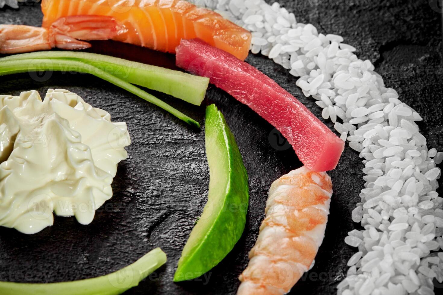 Circle of salmon, tuna, shrimp, avocado, rice and cream cheese on black surface photo