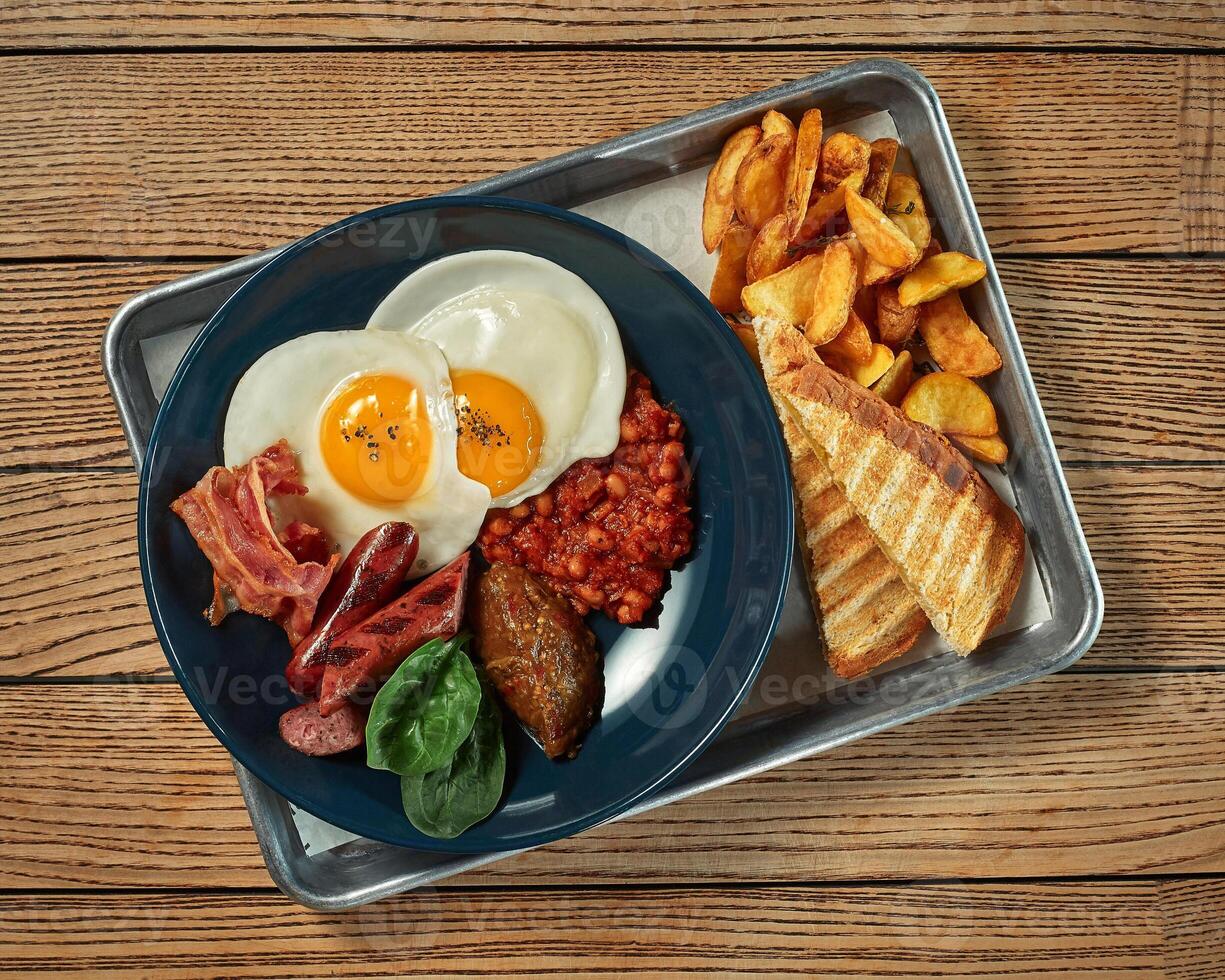 Breakfast with fried eggs, potatoes, stewed beans, bacon, sausages and toasts photo