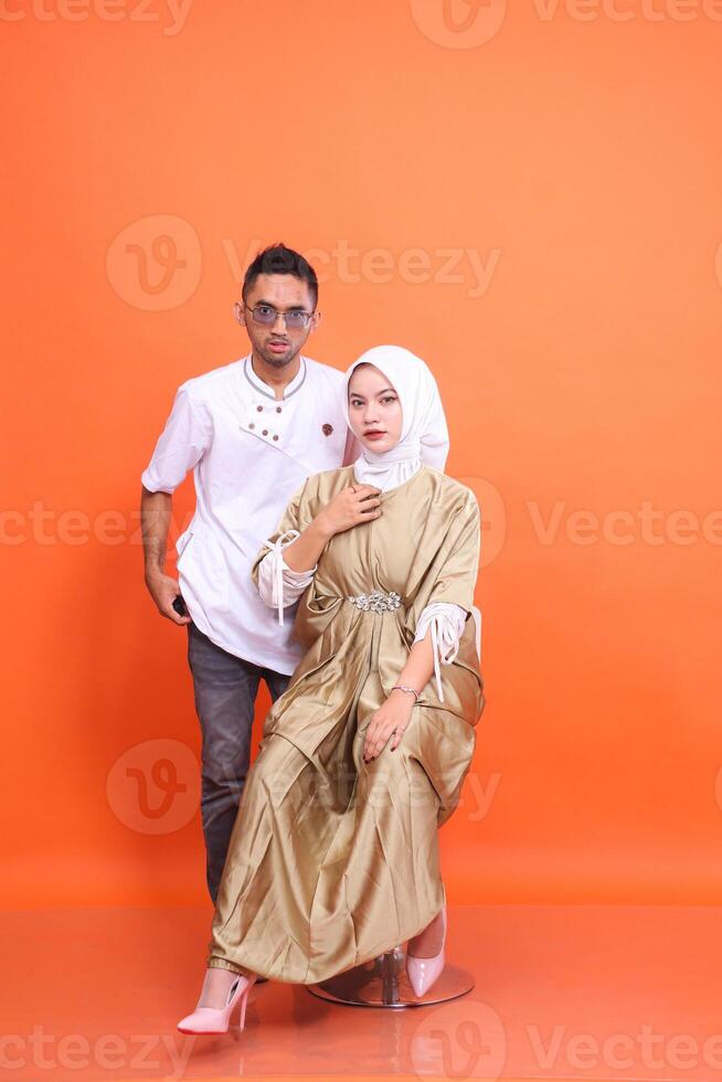 Asian muslim couple man and woman wearing kaftan and muslim clothes in the month of Ramadan isolated orange background. Islamic religious, fashion, advertising, commercial concepts photo