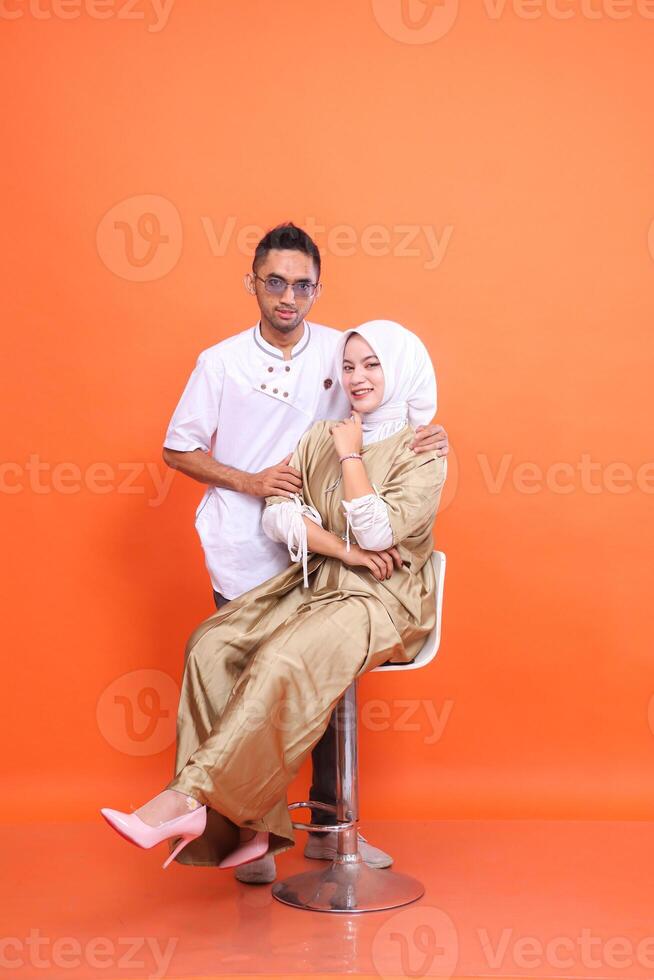 Full body of indonesia Muslim couple man and woman smiling leaning forward wearing kaftans and Muslim clothes in the month of Ramadan isolated on orange background. religious, advertising,commercial photo