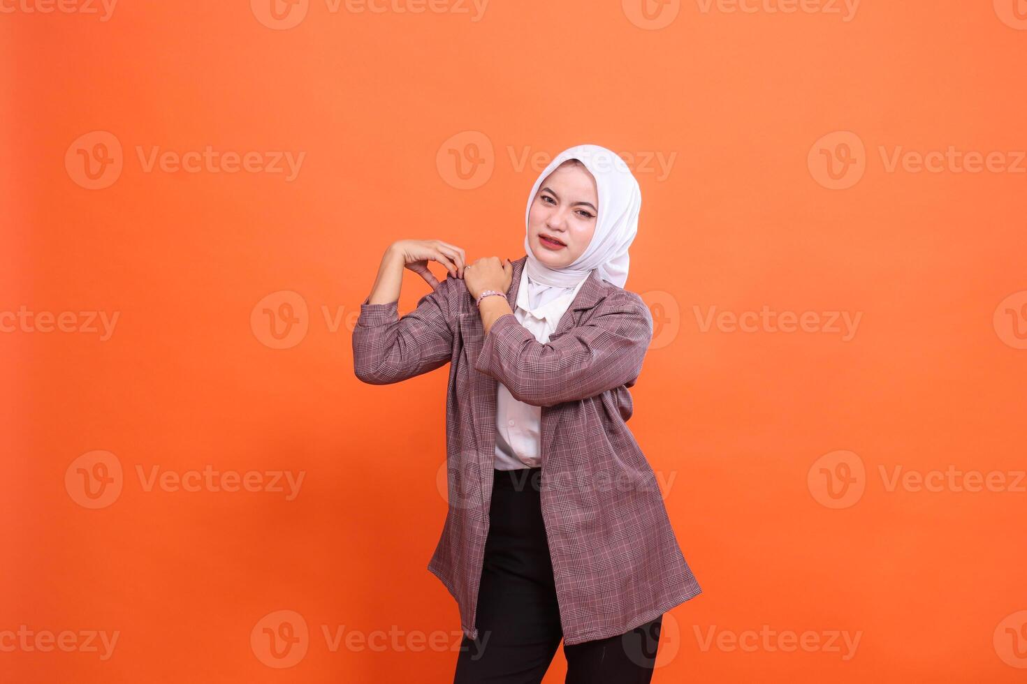 Portrait of beautiful young indonesia sick woman in hijab looking at the camera, Experiencing shoulder pain fatigue, putting hand on shoulder with orange studio background. Lifestyle, health care photo