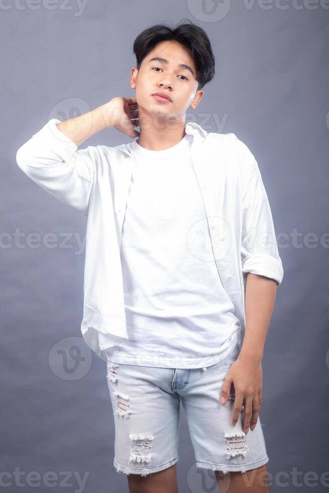 elegant asian man posing standing head straight ahead in front of the camera while his hands hold the back of the neck indoors. fashion promotion man shirt photo session in the gray background