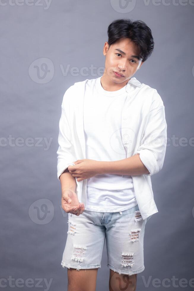 elegant asian man posing standing head straight in front of camera while hands buttoning shirt sleeves indoors. fashion promotion man shirt photo session in the gray background studio