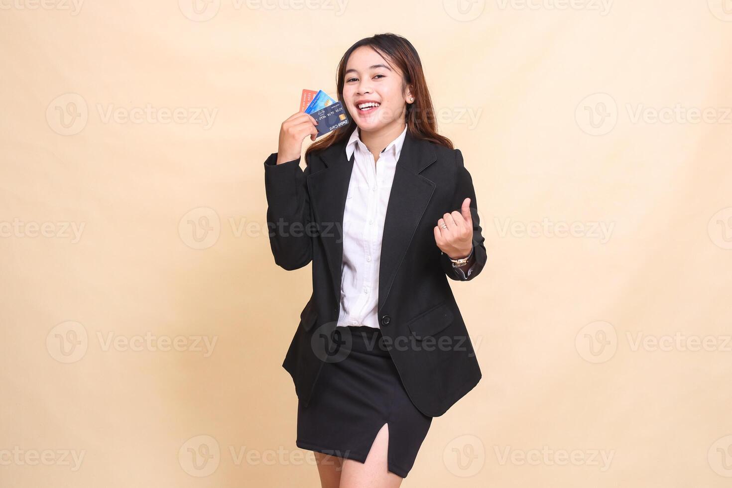 Beautiful formal Asian office woman in suit standing cheerful happy holding debit credit card and clenching fist for transaction promotion on yellow background for commercial, vacancy and business photo