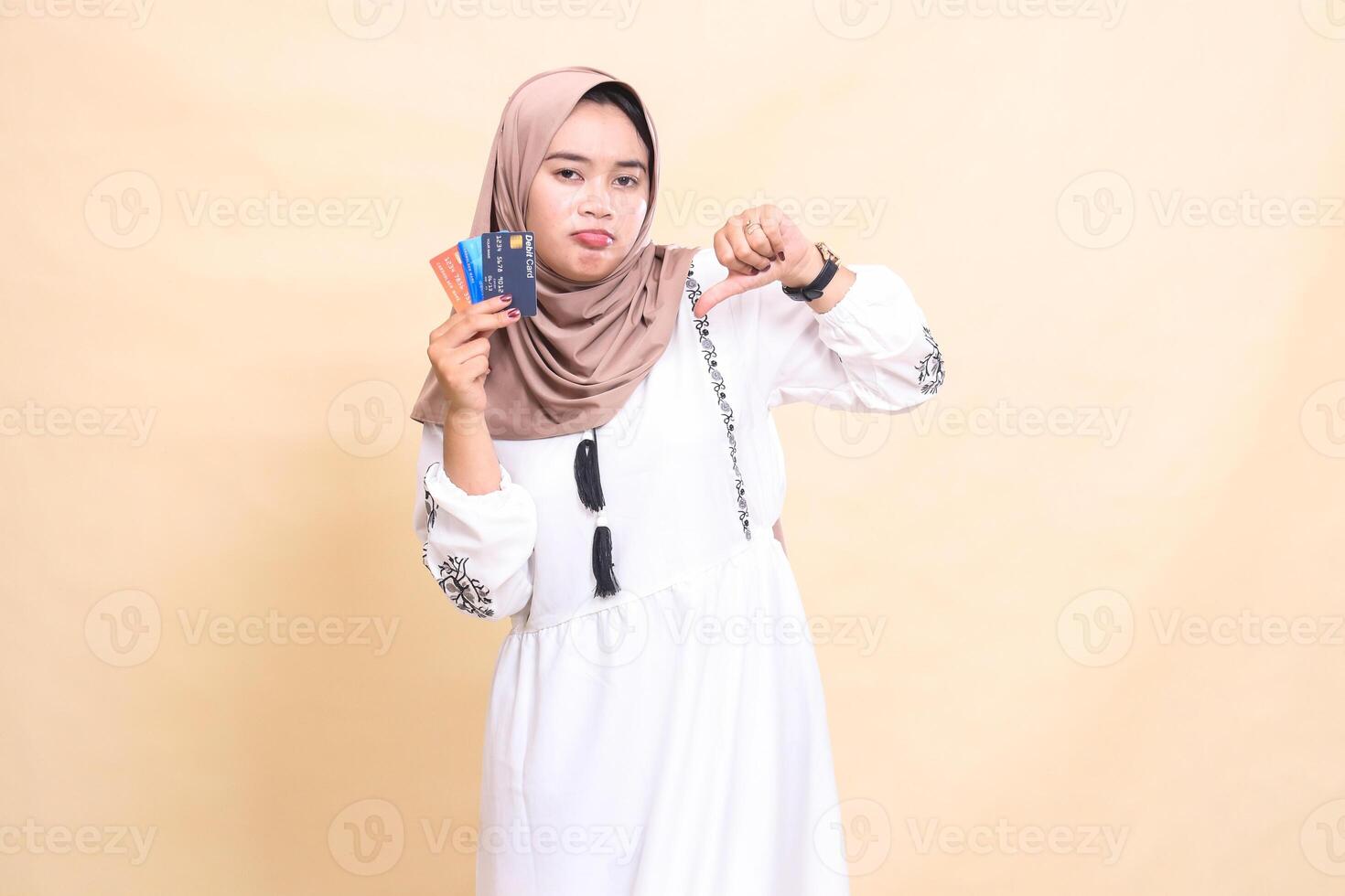 a beautiful indonesia Muslim woman in a hijab frowns with a thumbs up gesture and carries a debit credit card for offline online payments. used for advertising, technology, Eid and Ramadan photo
