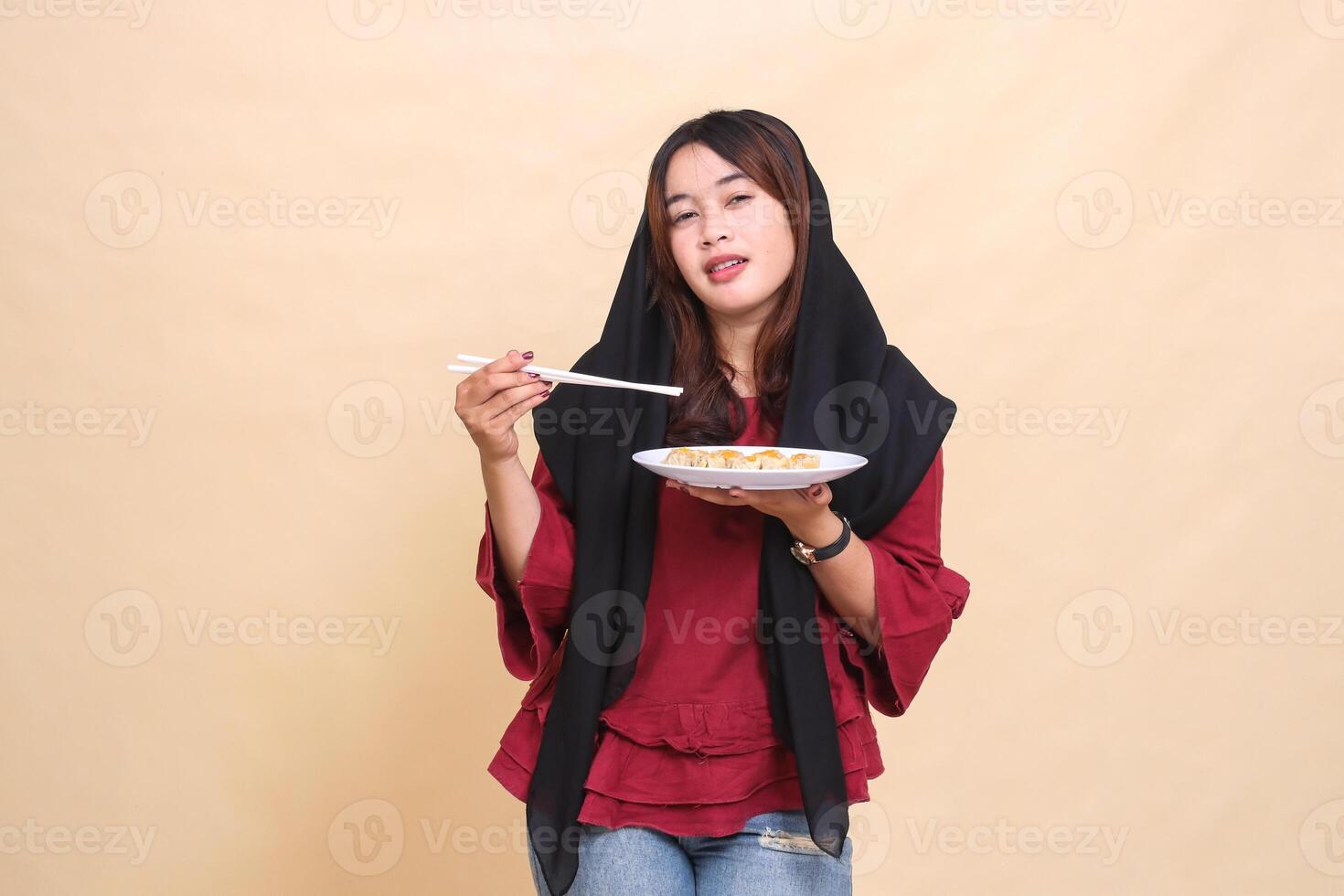 Beautiful mature indonesia girl wearing a red hijab with a weak expression, picking up chopsticks and carrying a plate containing dimsum Chinese food. used for food, health and lifestyle content photo