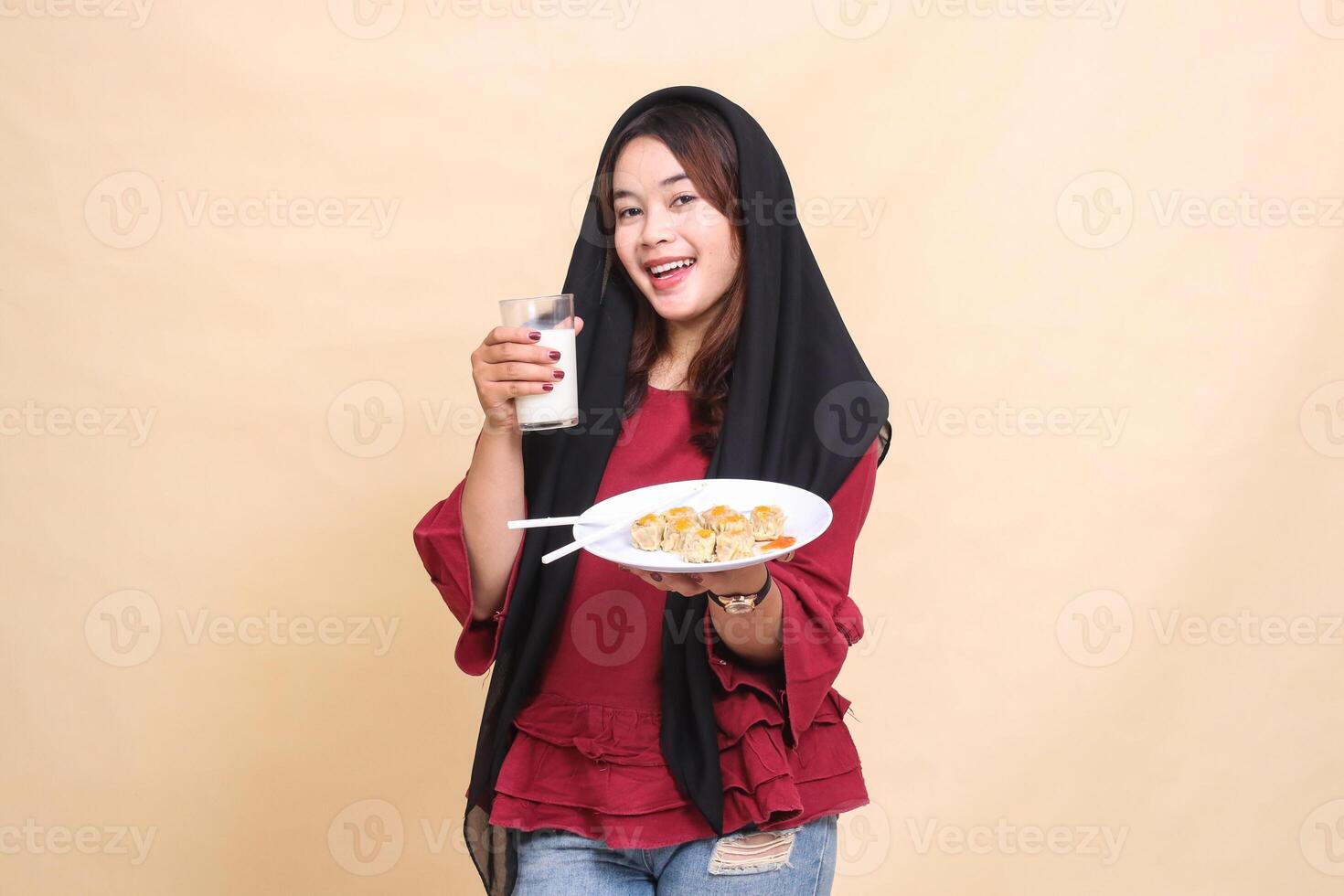 Beautiful elegant Asian woman in red shirt in hijab happy holding a glass of milk and carrying a plate containing dimsum Chinese food. used for food, beverage and culinary content photo