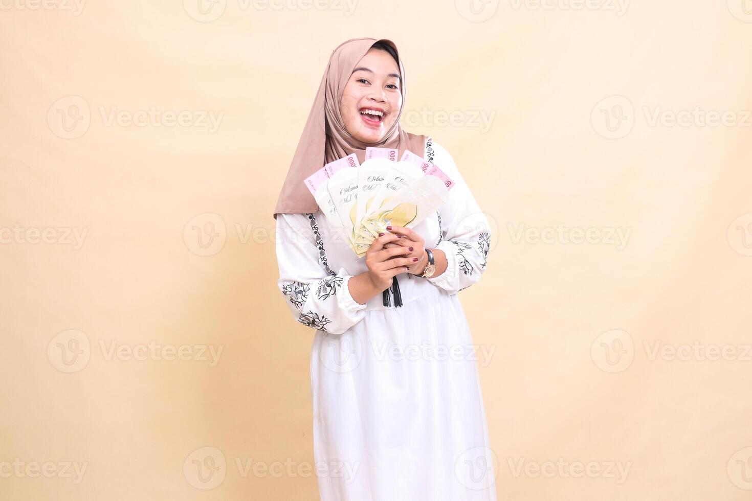 portrait of a beautiful Asian Muslim woman wearing a hijab smiling happily holding a gift or fitrah on Eid. used for advertising, giveaways, Eid and Ramadan photo