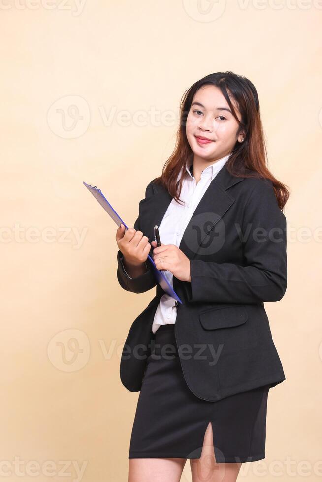 Beautiful formal Asian executive mature woman in suit arrogant smile standing and pose holding clipboard pen to camera, 3 by 4 body portrait on yellow background for commercial, vacancy and business photo