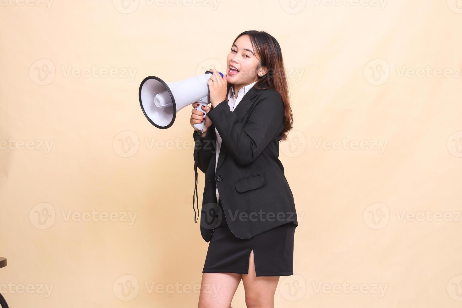 Beautiful formal Asian office woman in suit standing shouting using megaphone for broadcast announcement on yellow background for commercial, advertising and business photo