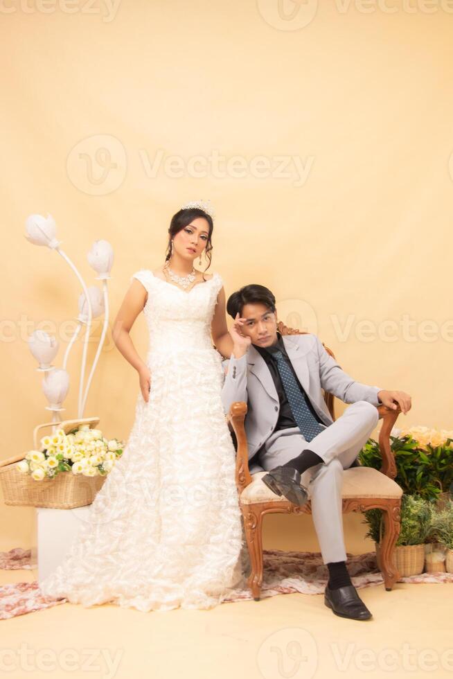 elegant male and female couple poses sitting on lounge chairs all women standing smiling slightly looking forward intimately indoor photo shot. couple wedding national bride studio
