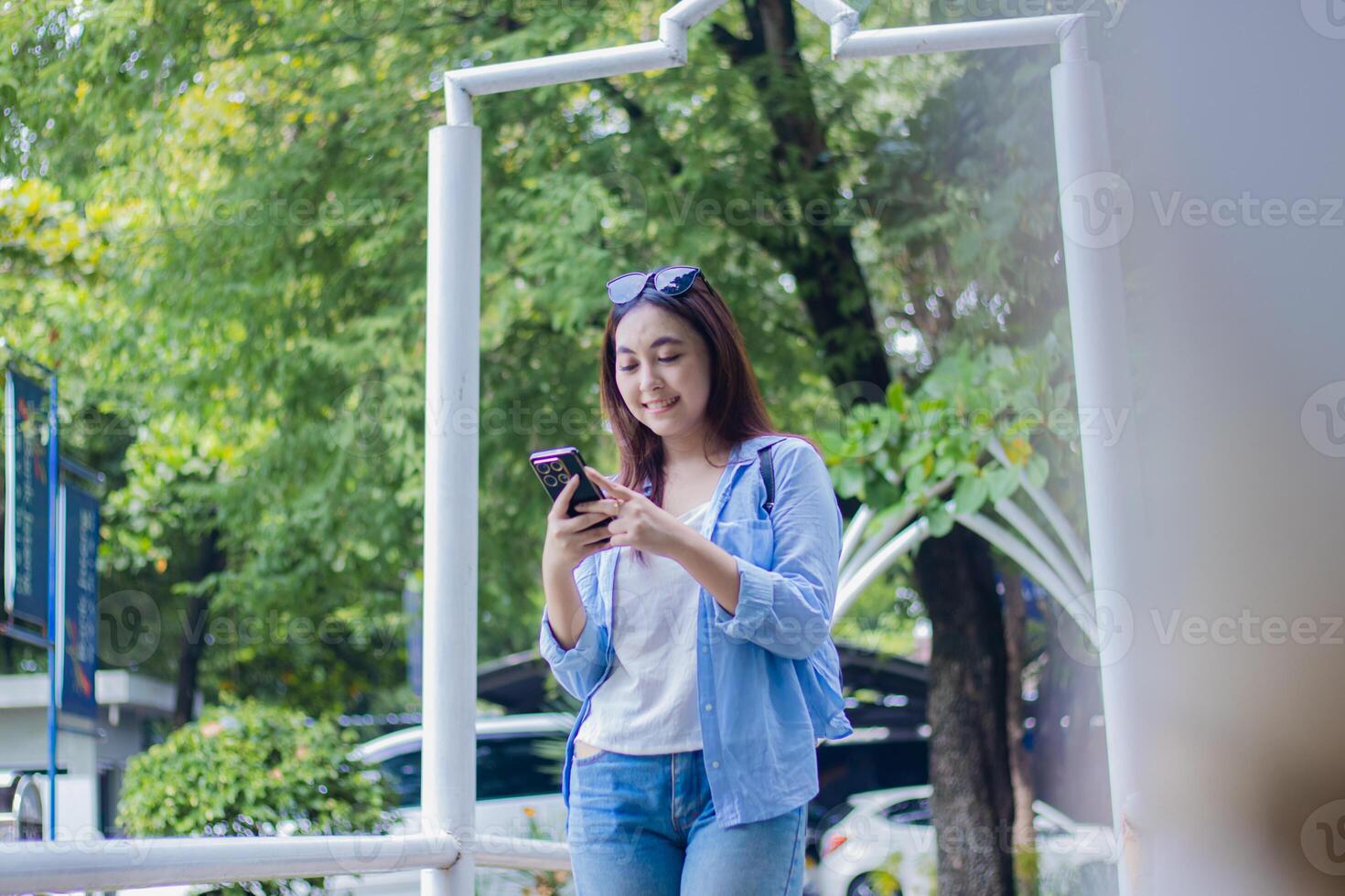 Beautiful Asian woman smiling using smart phone gadget glasses in campus park in sunny weather. female student for education, promotion and lifestyle concept photo