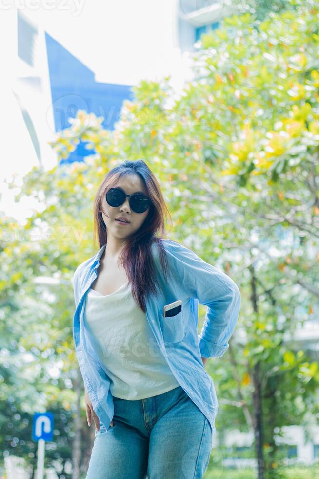 elegance indonesia woman in elegant sunglasses sexy looking at the camera holding her buttocks standing on outdoor park path. female students for the themes of education, fashion and lifestyle photo