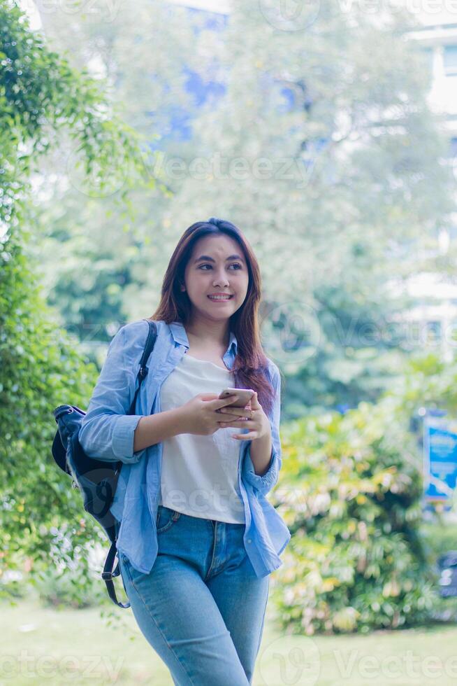 Beautiful candid smiling Asian woman using smart phone in park on sunny summer day. female students for education, promotion and lifestyle concepts photo
