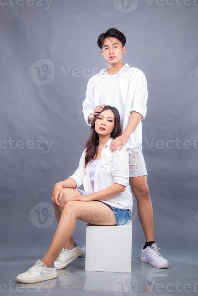 elegant men and women are posing standing and sitting in front of the camera while the ladder holding the shoulders and hair facing forward in the indoor.fashion promotion couple photo session in gray