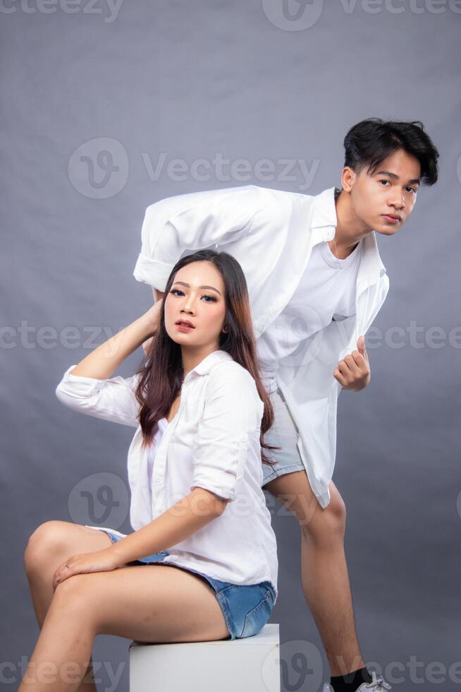 elegant men and woman posing standing in front of the camera while the ladder holding the hair in the indoor. fashion promotion couple shirt photo session in gray background studio