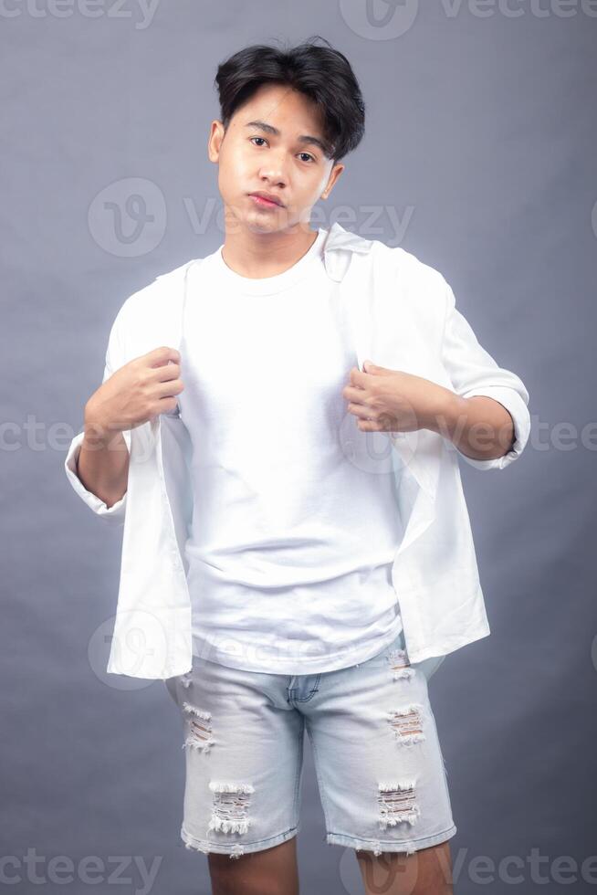 indonesia asian man posing standing with his head straight forward in front of the camera while holding his shirt in both hands. fashion promotion man shirt photo session in the gray background studio