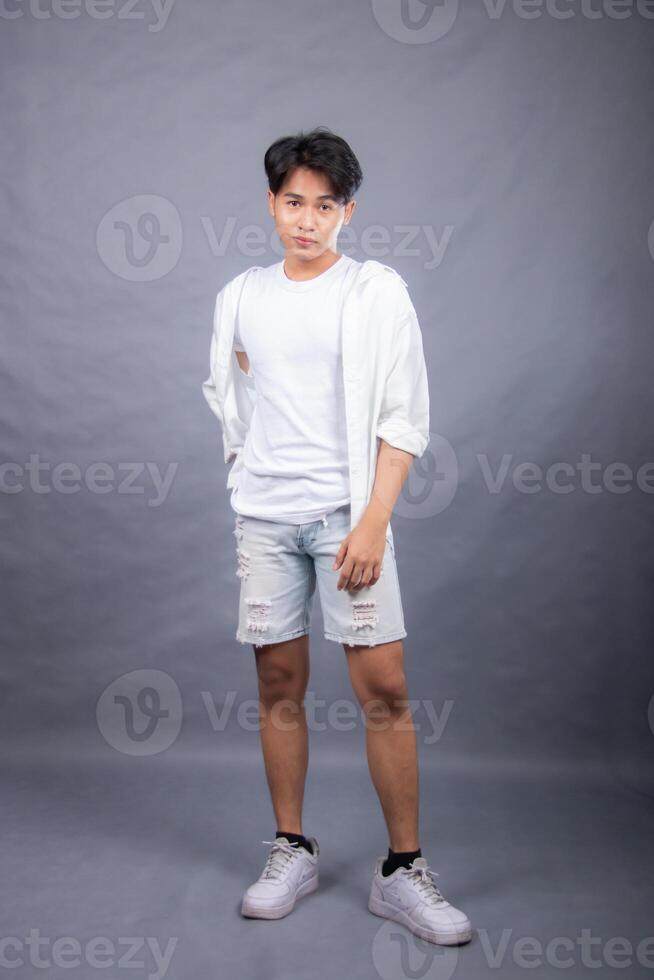 elegant asian man indonesian posing standing in front of the camera with his hands back indoors. fashion promotion man shirt photo session in the gray background studio