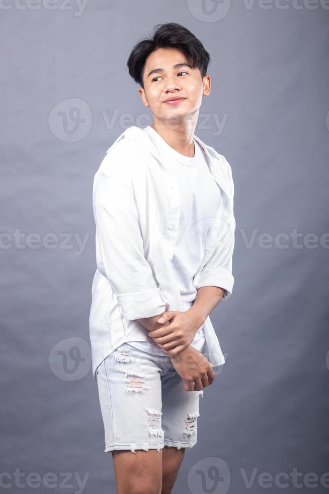 cool asian man posing standing head to right in front of the camera while his ladder is holding each other indoors. fashion promotion man shirt photo session in the gray background studio