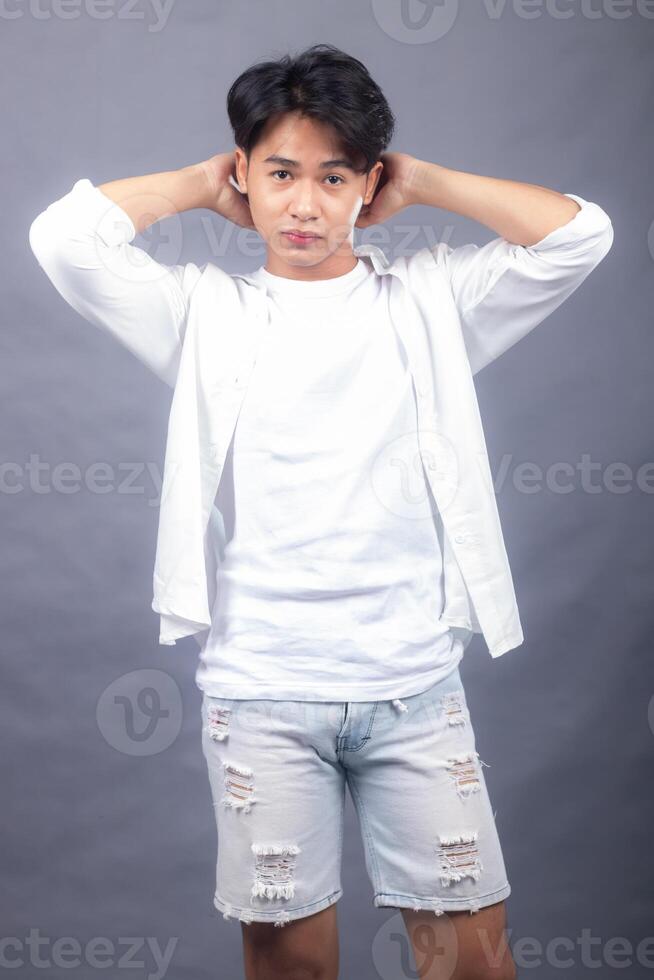 smart asian man posing standing head straight in front of the camera while holding his hair back indoors. fashion promotion man shirt photo session in the gray background studio