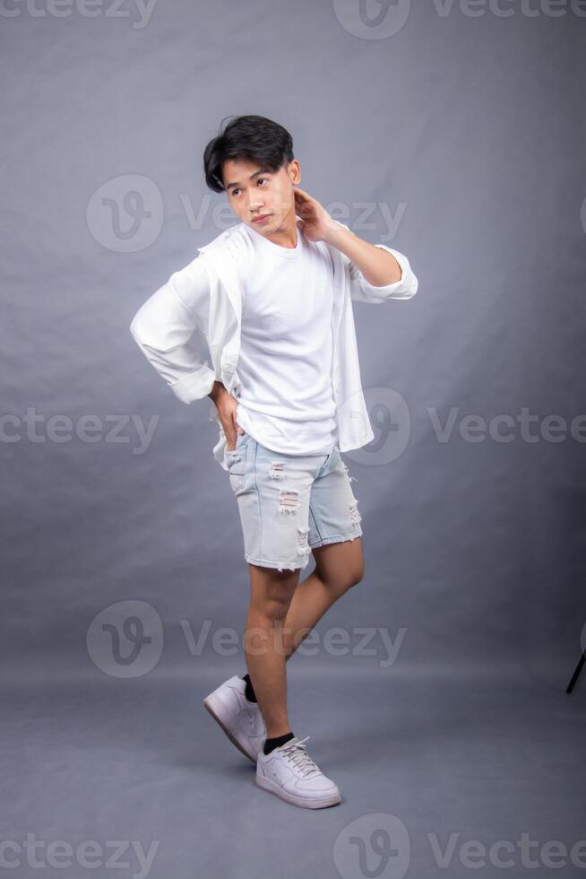 elegant asian man posing standing straight head to side in front of camera while hands back indoors. fashion promotion man shirt photo session in the gray background studio