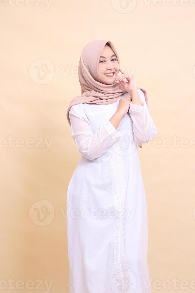 woman asian hijab wearing beautiful Muslim dress cheerful poses hands holding front of shoulders isolated on cream background. beauty, model, studio and fashion concept photo