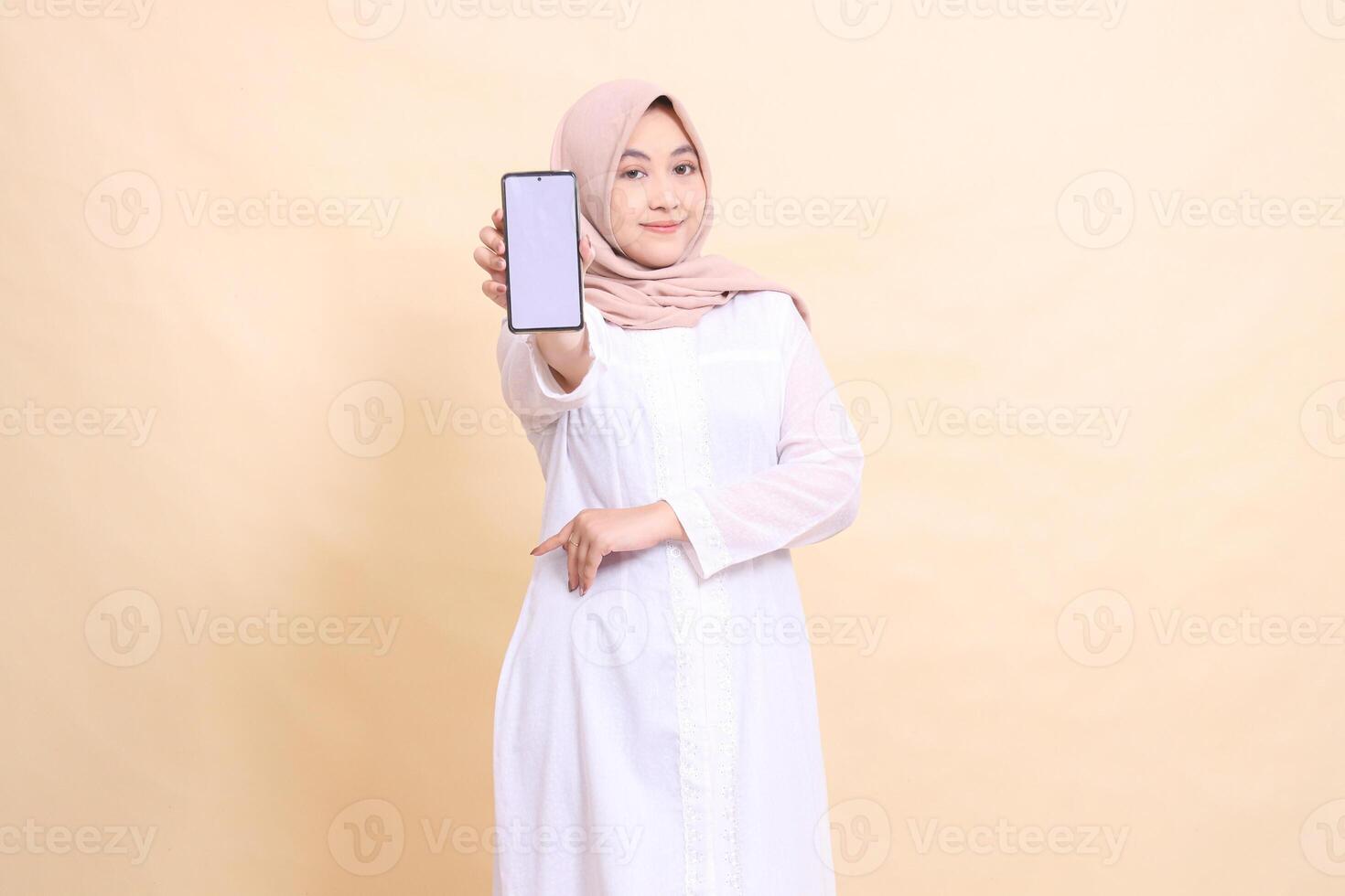 woman indonesia muslim wearing a hijab smiling, holding a cellphone gadget in her hand in front of her with her arms crossed. Lifestyle, business and finance concept photo