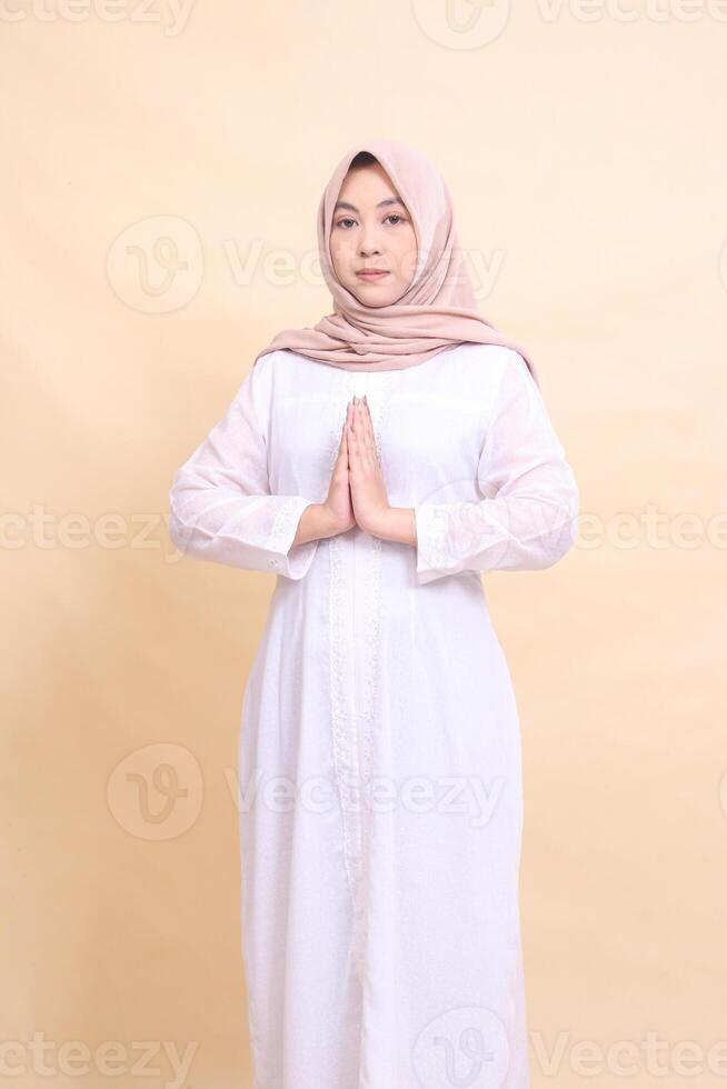 Asian woman wearing beautiful elegant Muslim dress poses with arms crossed isolated on cream background. beauty, model, studio and fashion concept photo