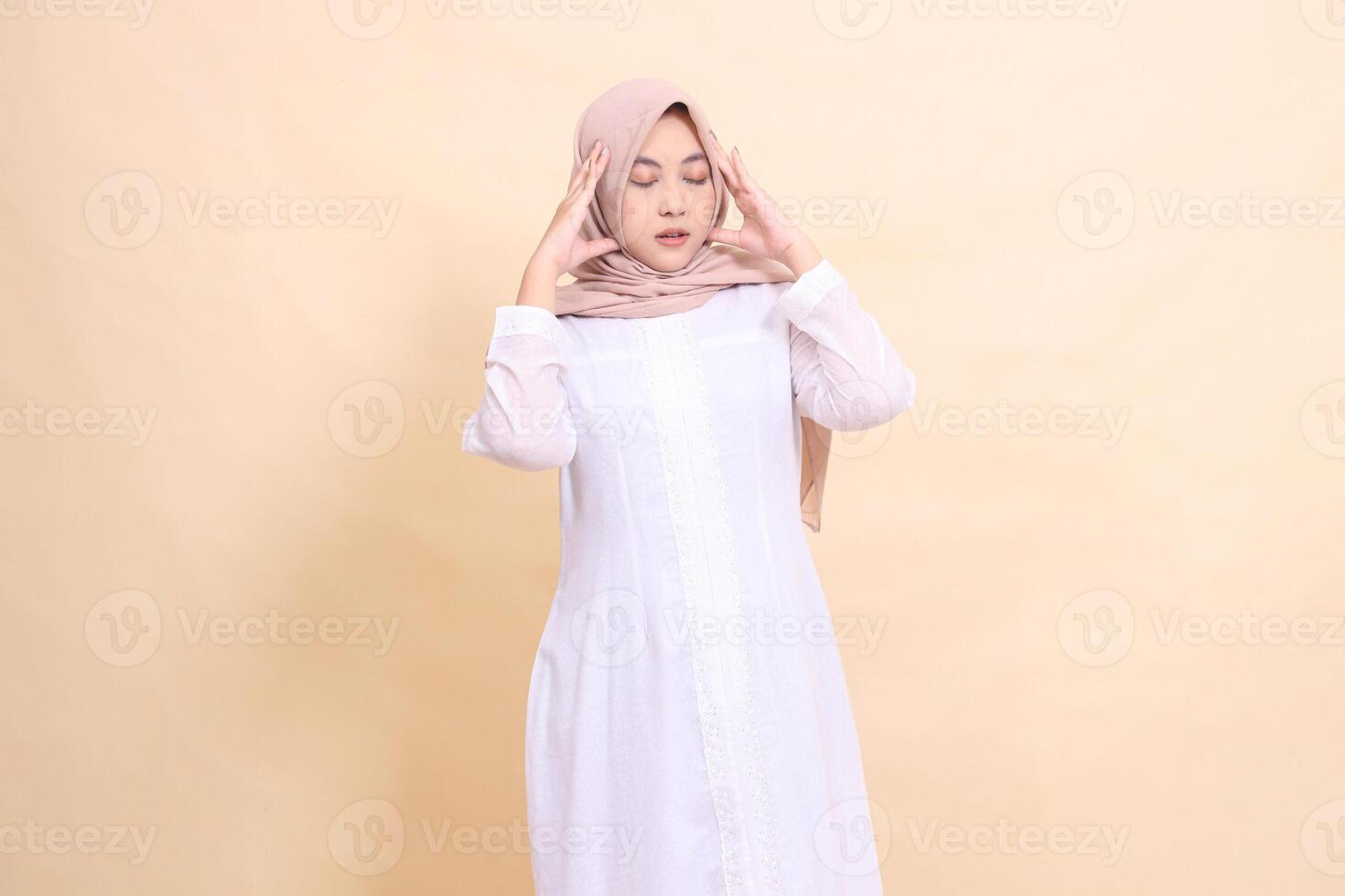 An girl asian wearing a white dress and brown hijab stands candidly with her hands holding her sick head. for health, care, education and science concepts photo