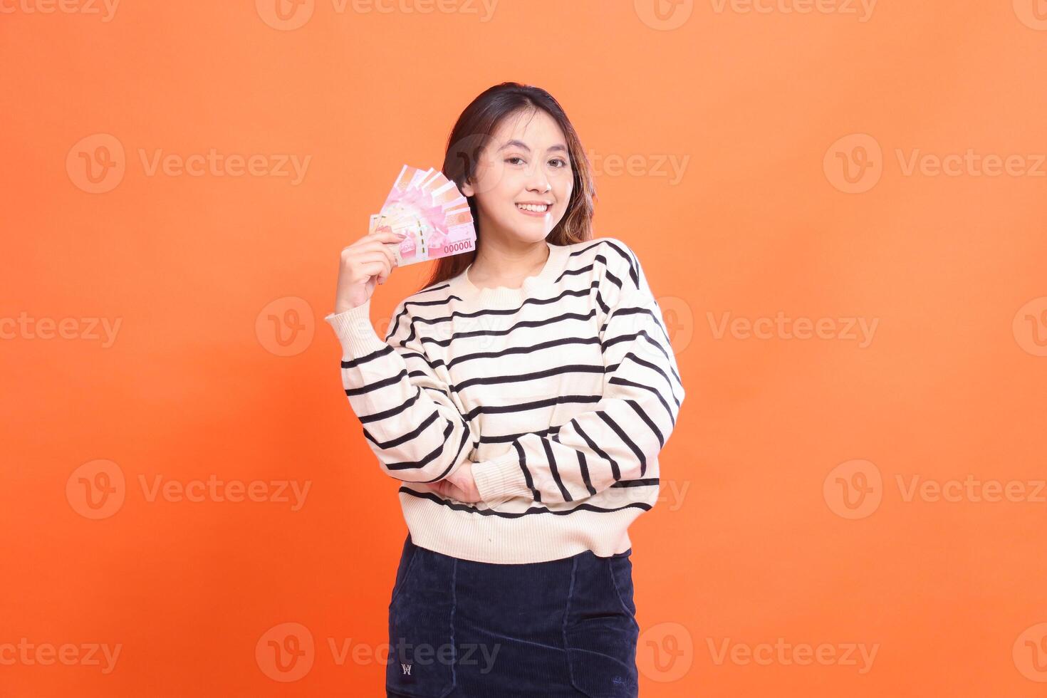The expression of a cheerful Asian woman standing while holding a number of rupiah bills in her arms. for fashion, business and finance concept photo