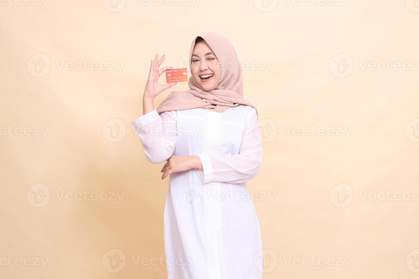 woman indonesia muslim in hijab smiling cheerfully holding a debit credit card in her hand with her arms crossed. Lifestyle, business and finance concept photo
