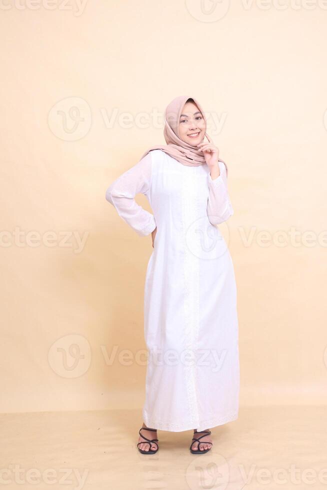 full body girl indonesia wearing beautiful dress cheerful pose holding waist and cheeks isolated on cream background - beauty, model, studio and fashion concept photo