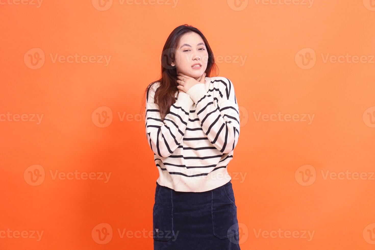 Beautiful mature asian woman at camera suffering from pain in throat after consuming food and drink isolated on orange background photo
