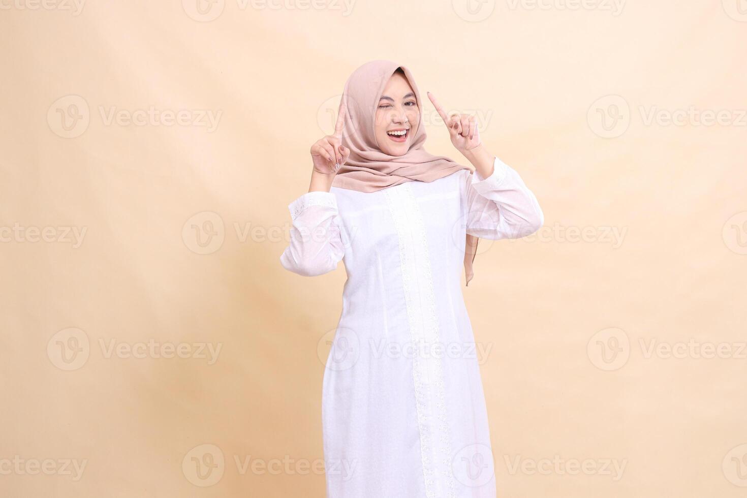 woman indonesia muslim standing to the camera smile happy both hands pointing up. Fashion, pointer, business and promotion concept photo