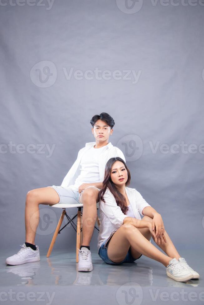 elegant men and women posing sitting in front of the camera while leaning back indoors. fashion promotion couple photo session in gray background studio
