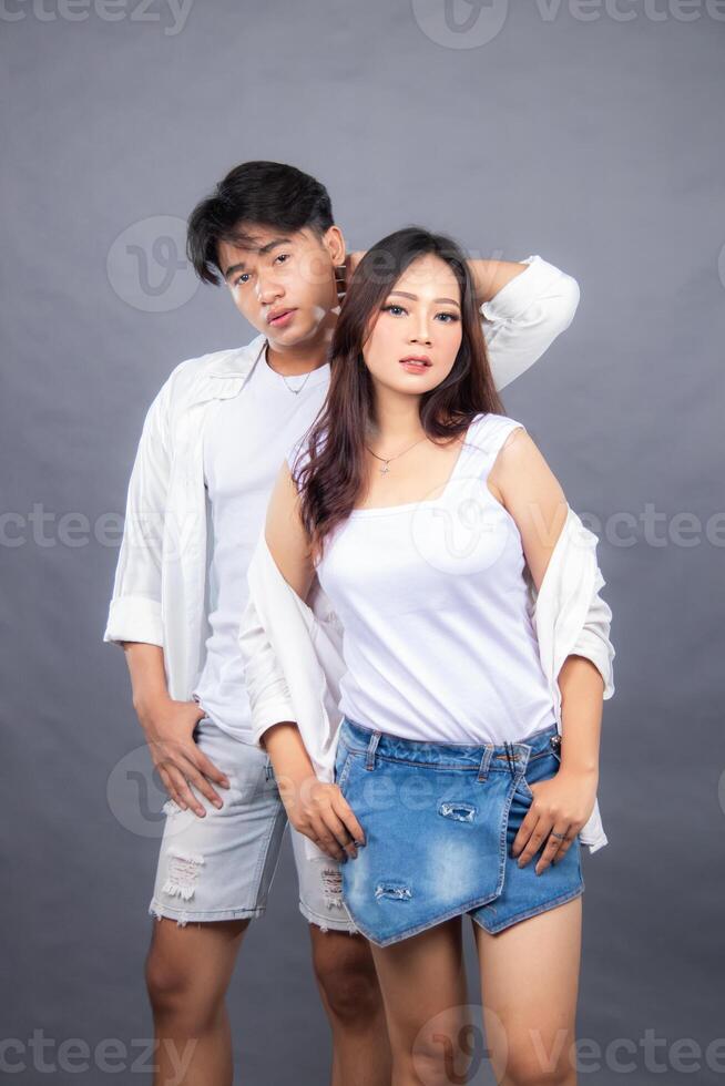 elegant men and women posing standing in front of the camera while the ladder holding the hair and jeans in the indoor. fashion promotion couple shirt photo session in gray background studio