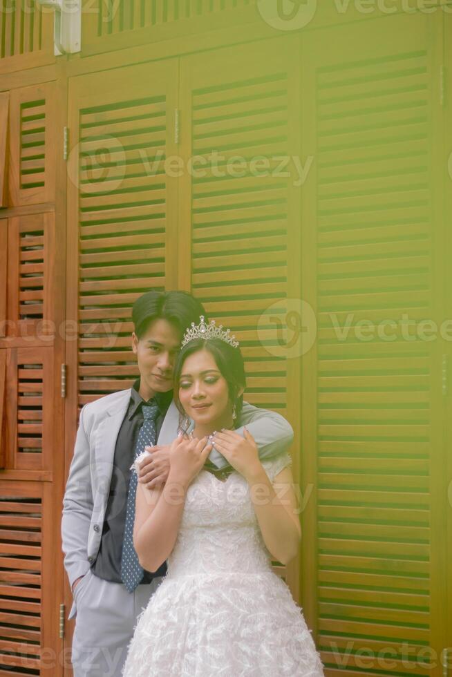 a pair of men and women in elegant poses standing laughing with men hands embracing from behind the woman's body while closing her eyes wearing a beautiful dress in a park photo shot medium shoot
