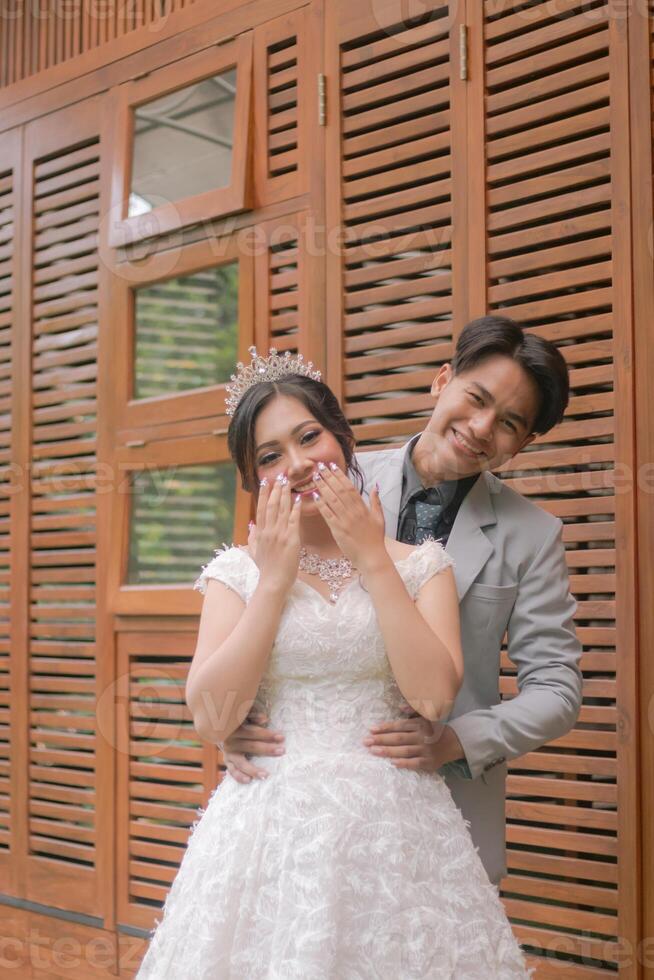 a pair of man and woman in elegant poses standing laughing with women's hands covering their mouths wearing beautiful dresses in a park photo shoot