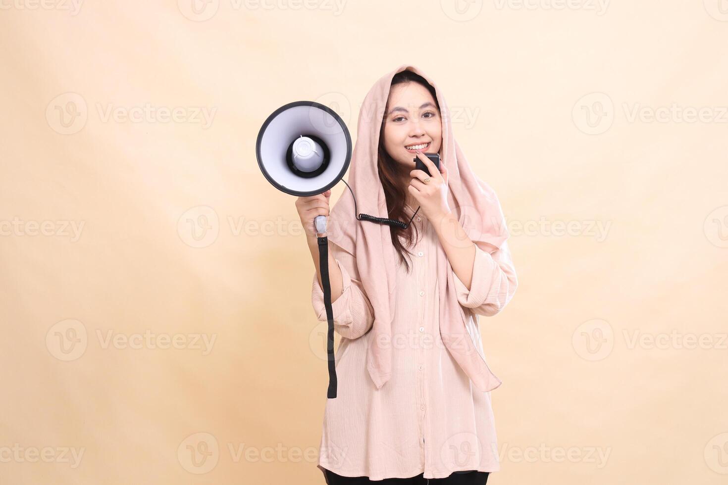 Asian woman looking at camera holding audio and holding megaphone loudspeaker smiling to announce announcement. young beautiful for business, technology, fashion photo