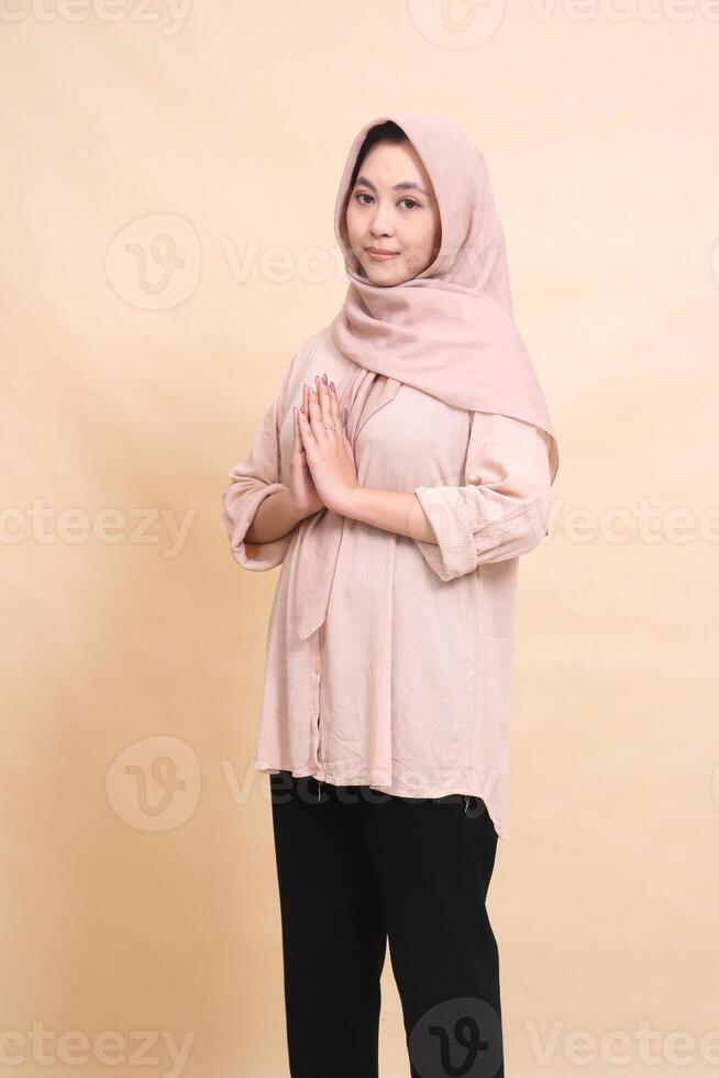 Asian Muslim woman wearing a hijab standing at an angle to the right smiling with her hand gesturing to welcome the month of fasting sawadikap and Eid al-Fitr. beautiful women for fashion, lifestyle photo
