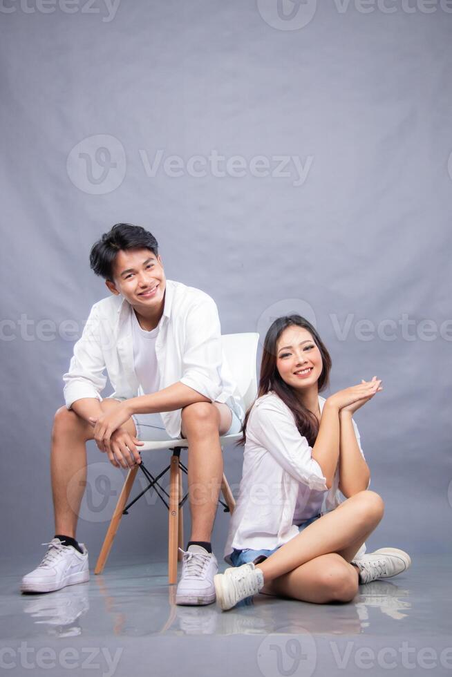 cheerful smiling man and woman posing sitting in front of camera while ladder holding each other indoors. fashion promotion couple photo session in gray background studio