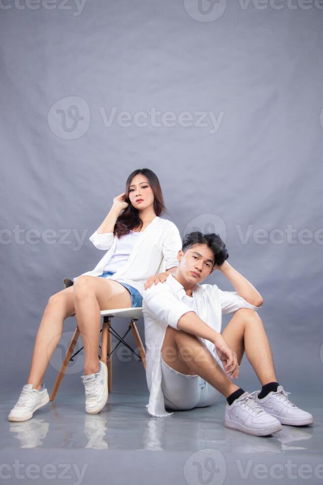 elegant men and women posing sitting in front of the camera while the ladder holding the hair facing forward in the indoor. fashion promotion couple photo session in gray background studio