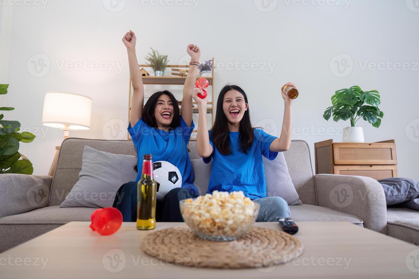 Lesbian couple cheering for Euro football with drinks and popcorn at home. Concept of sports enthusiasm and LGBTQ pride photo