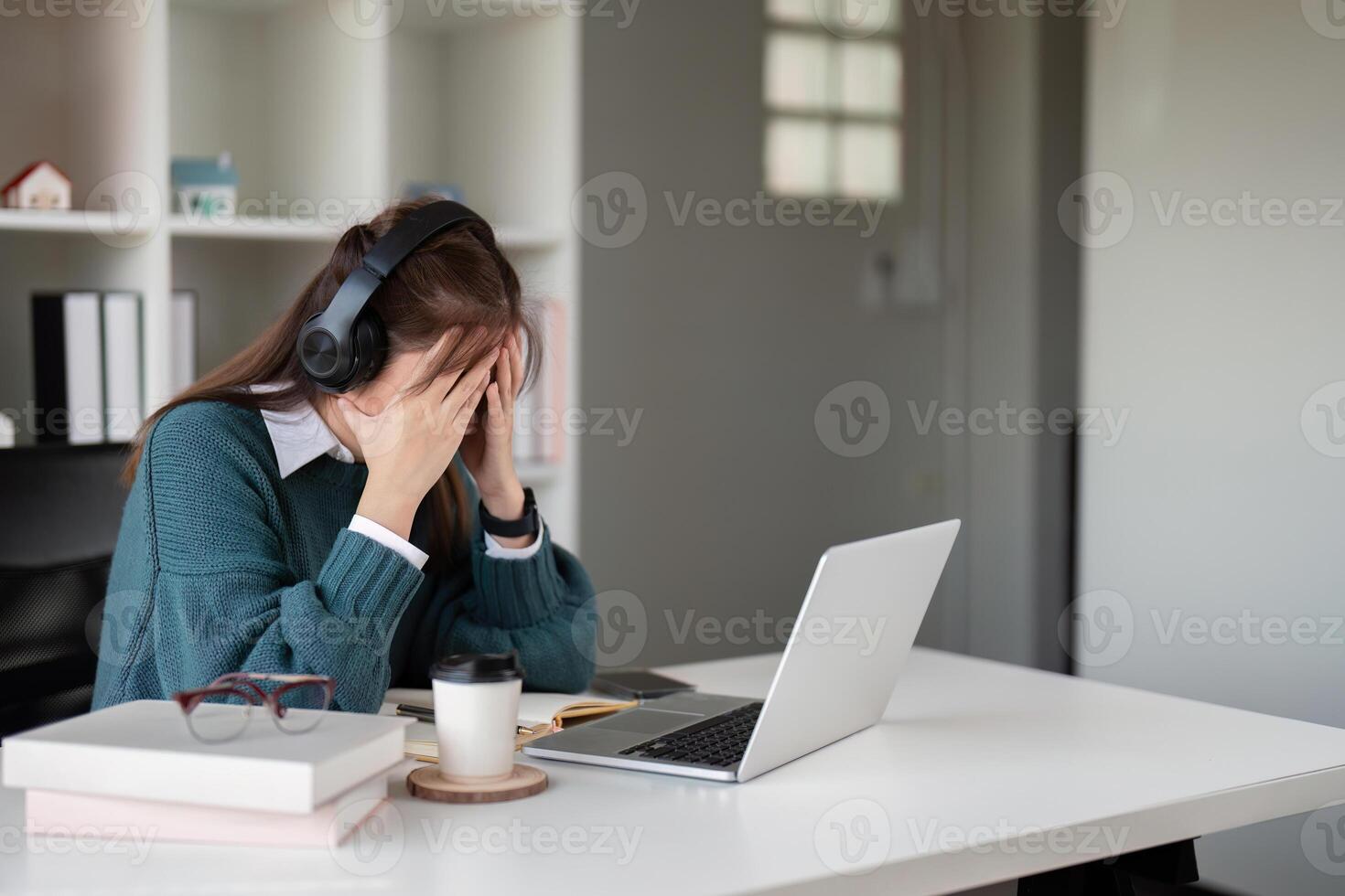 Young woman feeling stressed while wearing headphones and using a laptop in a home office photo