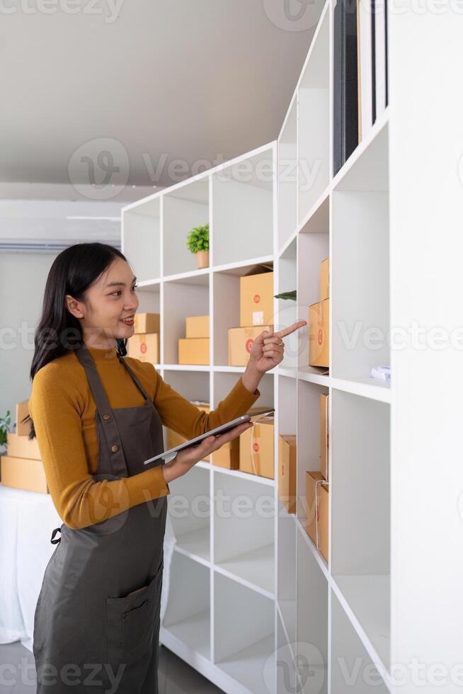 Ecommerce business owner managing inventory and checking stock in home office. Small business entrepreneur organizing packages for shipment and using a tablet for inventory tracking photo