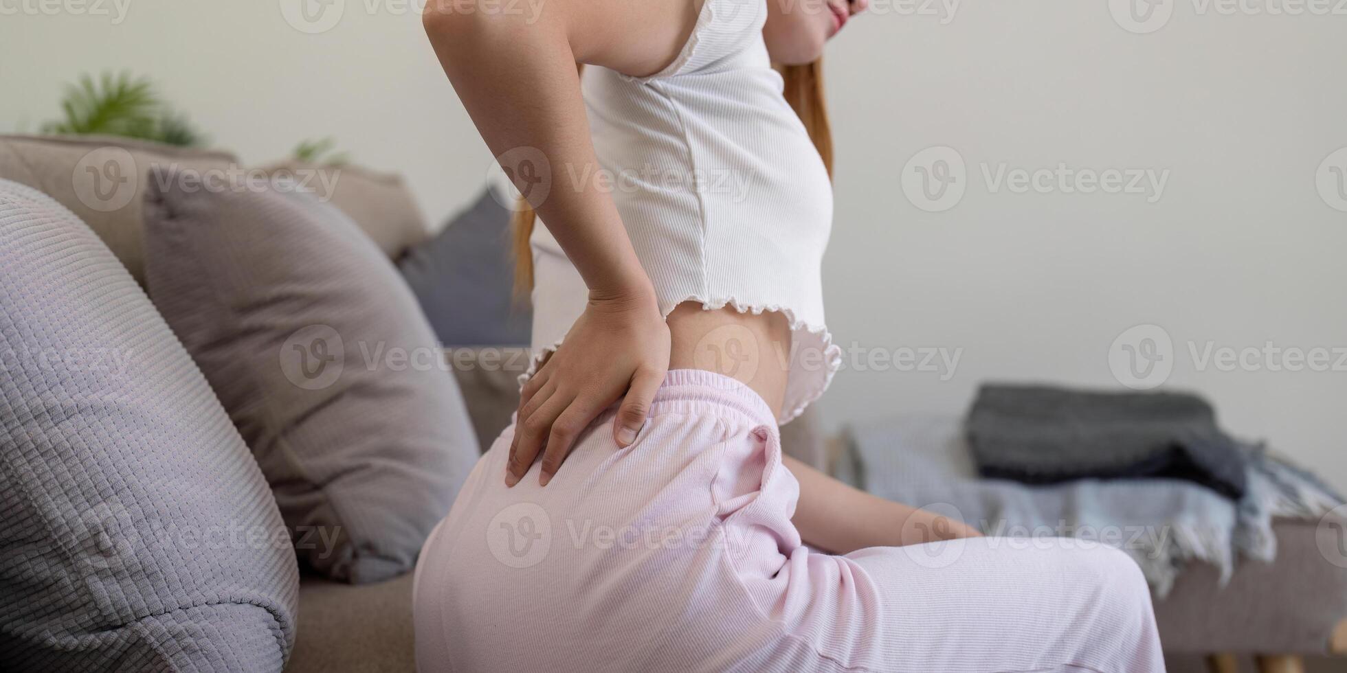 Asian woman having backache and touching her back in living room at home photo